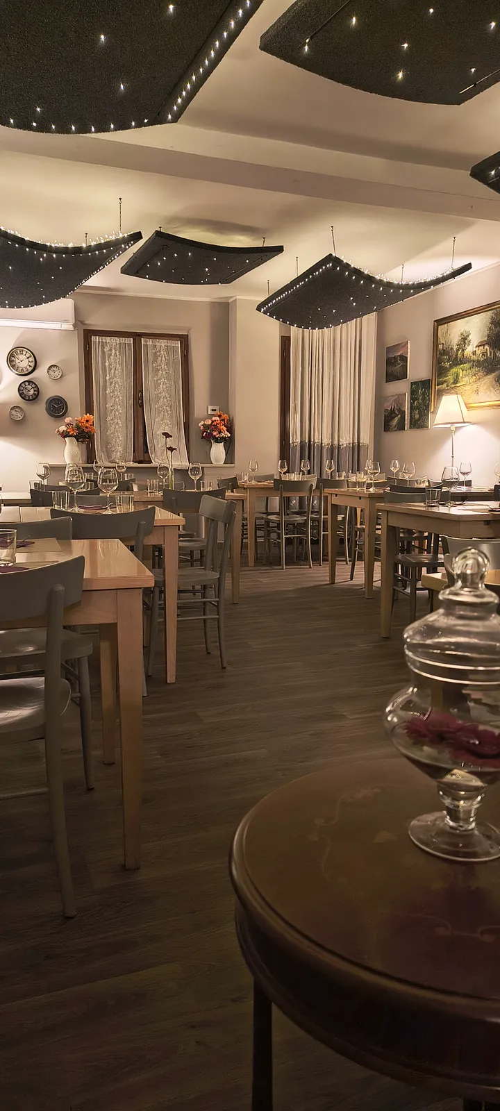 La sala dell’osteria di sera La sala dell’osteria di sera, con le luci soffuse sul soffitto e i tavoli apparecchiati