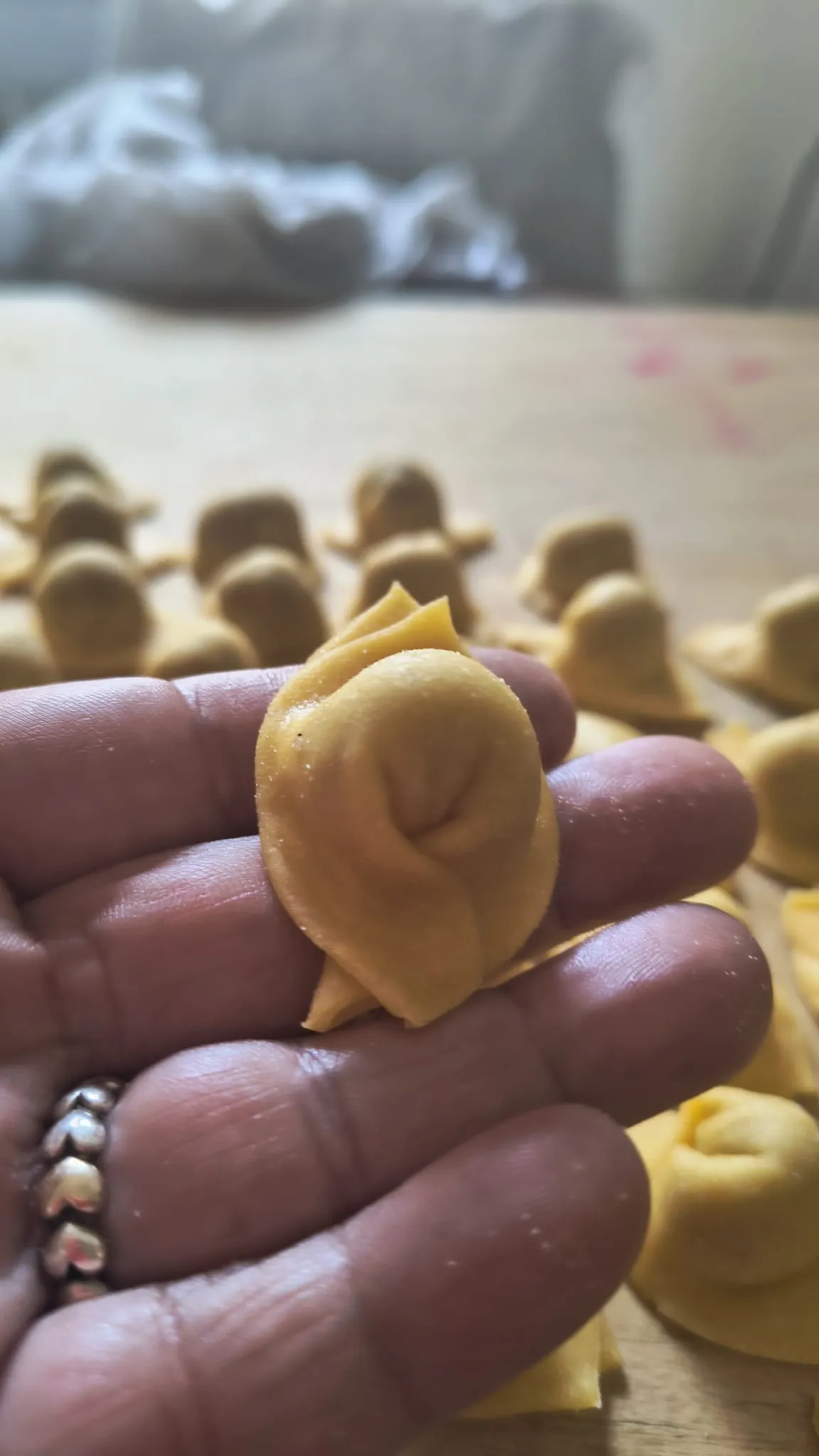 Un tortello fresco tenuto in mano, con altri tortelli sullo sfondo Un tortello fresco tenuto in mano, con altri tortelli sullo sfondo